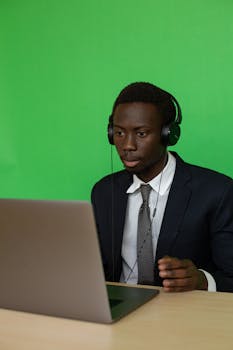 Business professional in formal attire engaged in video call against green screen backdrop.