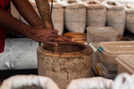 Close-up of hands grinding herbs in a wooden mortar at a São Paulo market stall.
